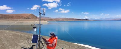 A man is standing next to a lake with a device in front of him.