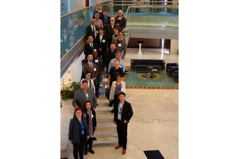 A group of people in business attire pose for a photo on an indoor staircase in a modern building with glass railings.