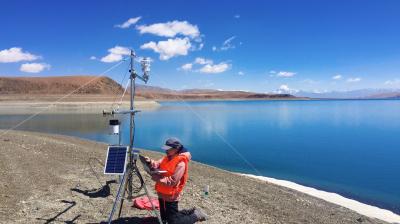 A man is standing next to a lake with a device in front of him.