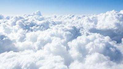 Fluffy white clouds fill the sky under a clear blue background, creating a soft, airy landscape from an aerial perspective.