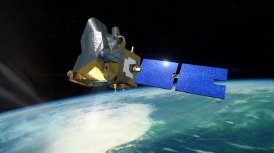 A satellite with blue solar panels orbits above Earth, with a view of clouds, land, and ocean below against the blackness of space.