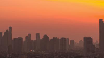 Silhouetted city skyline with numerous high-rise buildings under an orange and yellow sunset sky.