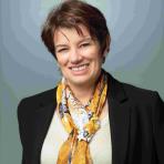 A person with short brown hair wearing a black blazer, beige top, and yellow scarf.